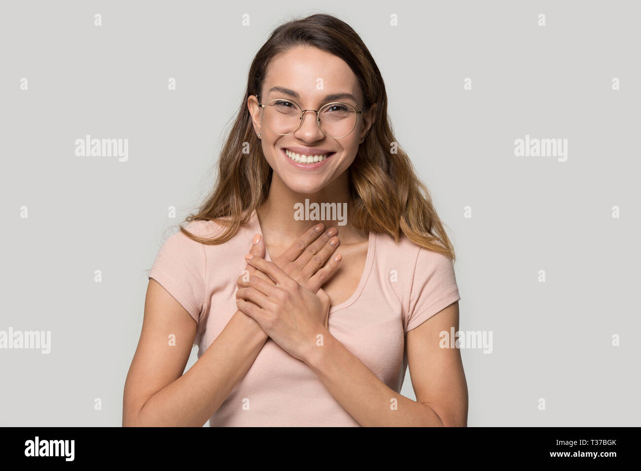 Headshot woman in glasses feels grateful holding hands on chest Stock Photo