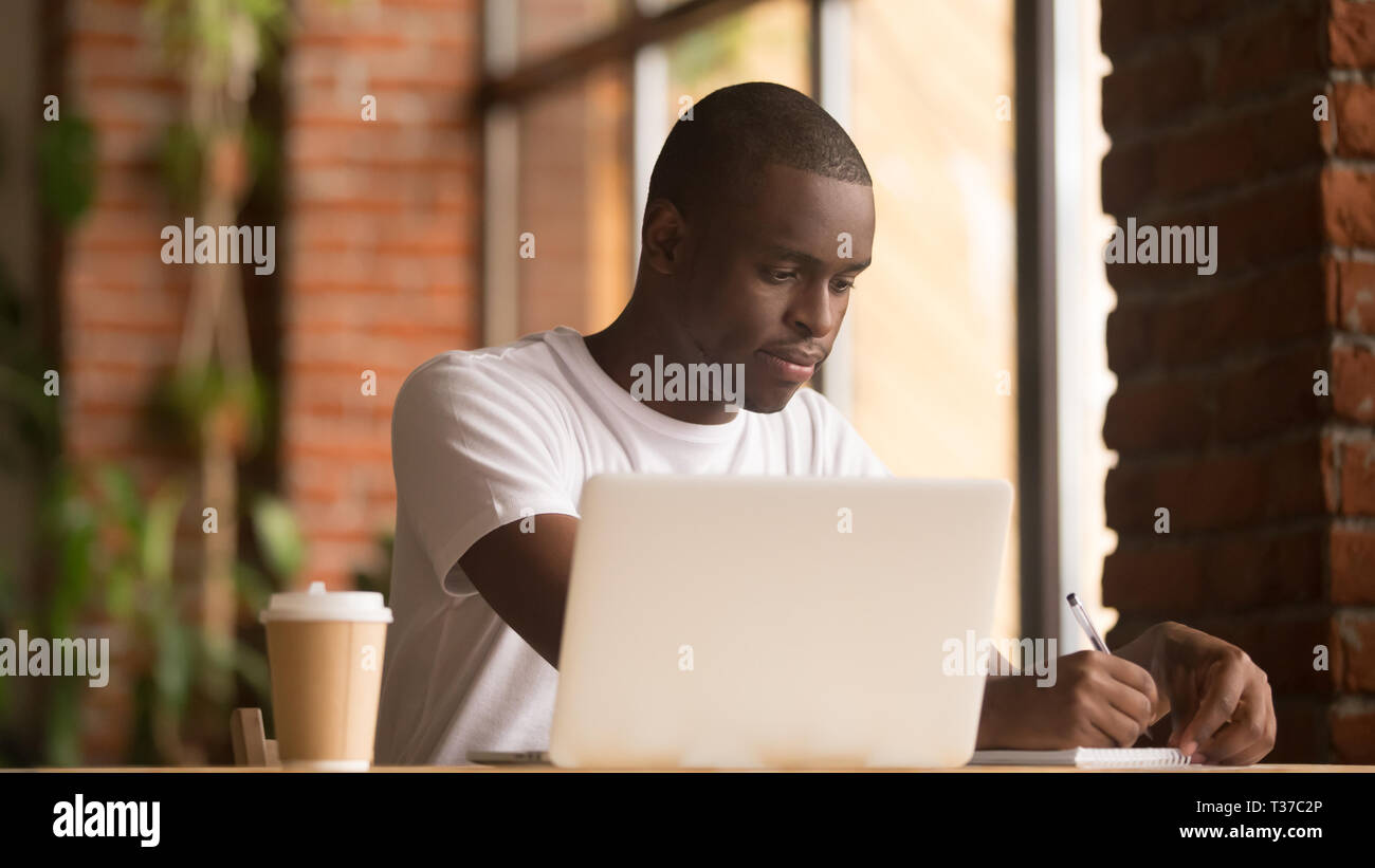 Serious african american man working studying with laptop making notes Stock Photo