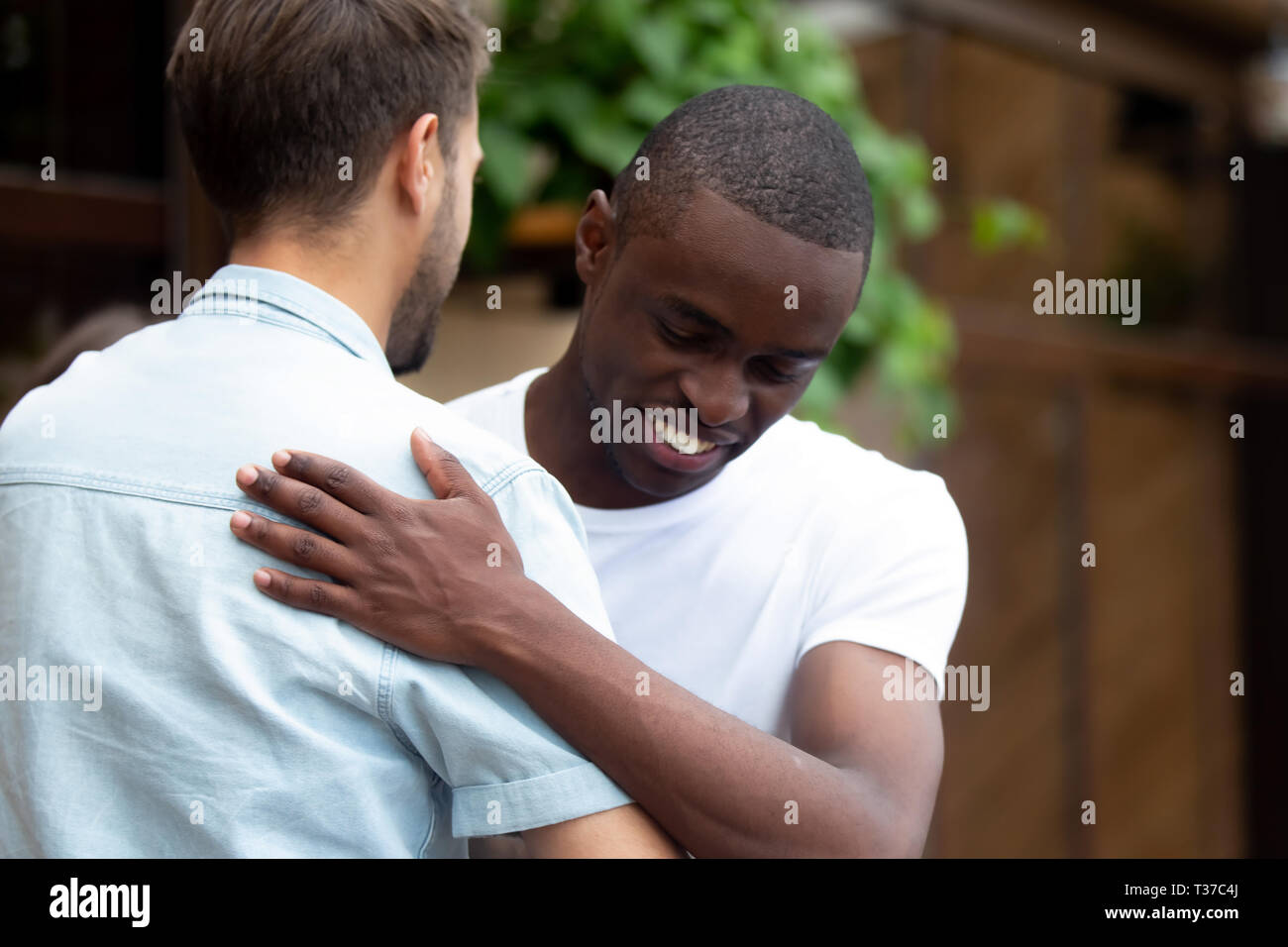 Happy two multiracial male best friends greeting embracing at meeting Stock Photo