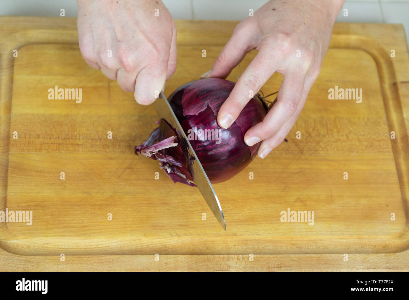 Close up of female slicing ends off of a red onion on a cutting board ...