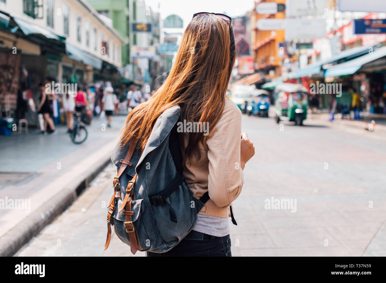 Rear view of young female tourist backpacker walking on Khao San road in summer during trip to Bangkok, Thailand Stock Photo