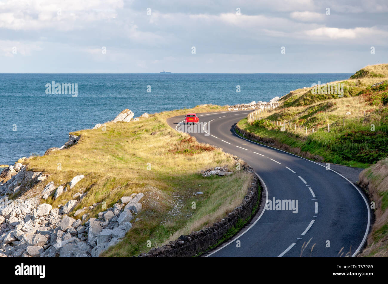 The eastern coast of Northern Ireland and Antrim Coastal Road, a.k.a.  Causeway Coastal Route with a red car. Sunset light Stock Photo - Alamy