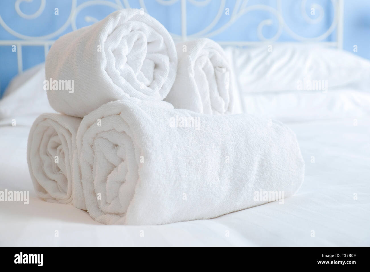 nicely rolled up clean and fresh towels lie on the white sheets of a steel bed in a beautifully lit hotel room Stock Photo