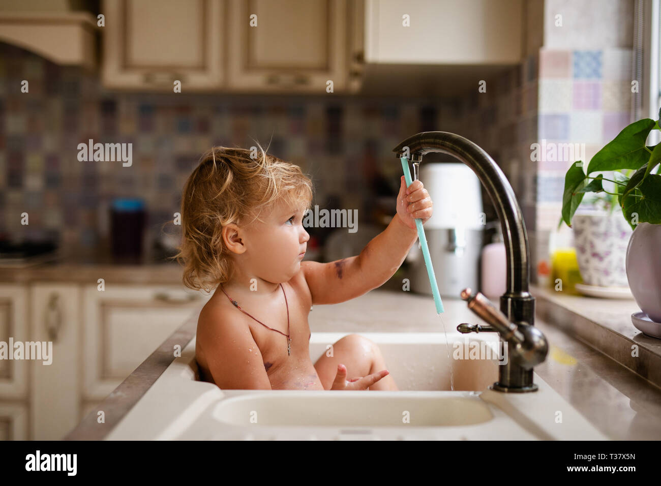 Baby taking bath in the kitchen sink. Child playing with water and soap