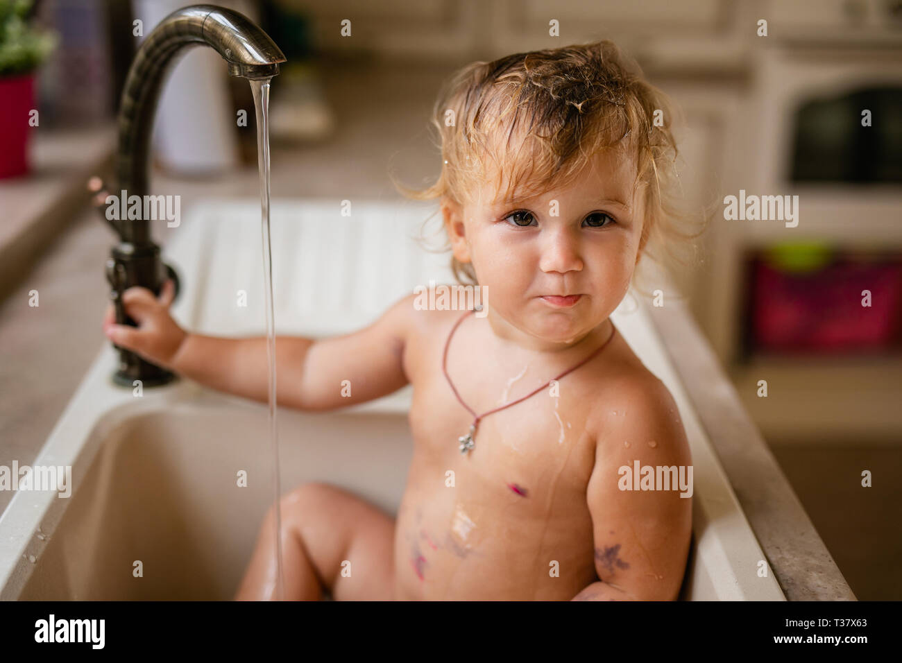 Baby taking bath in the kitchen sink. Child playing with water and soap