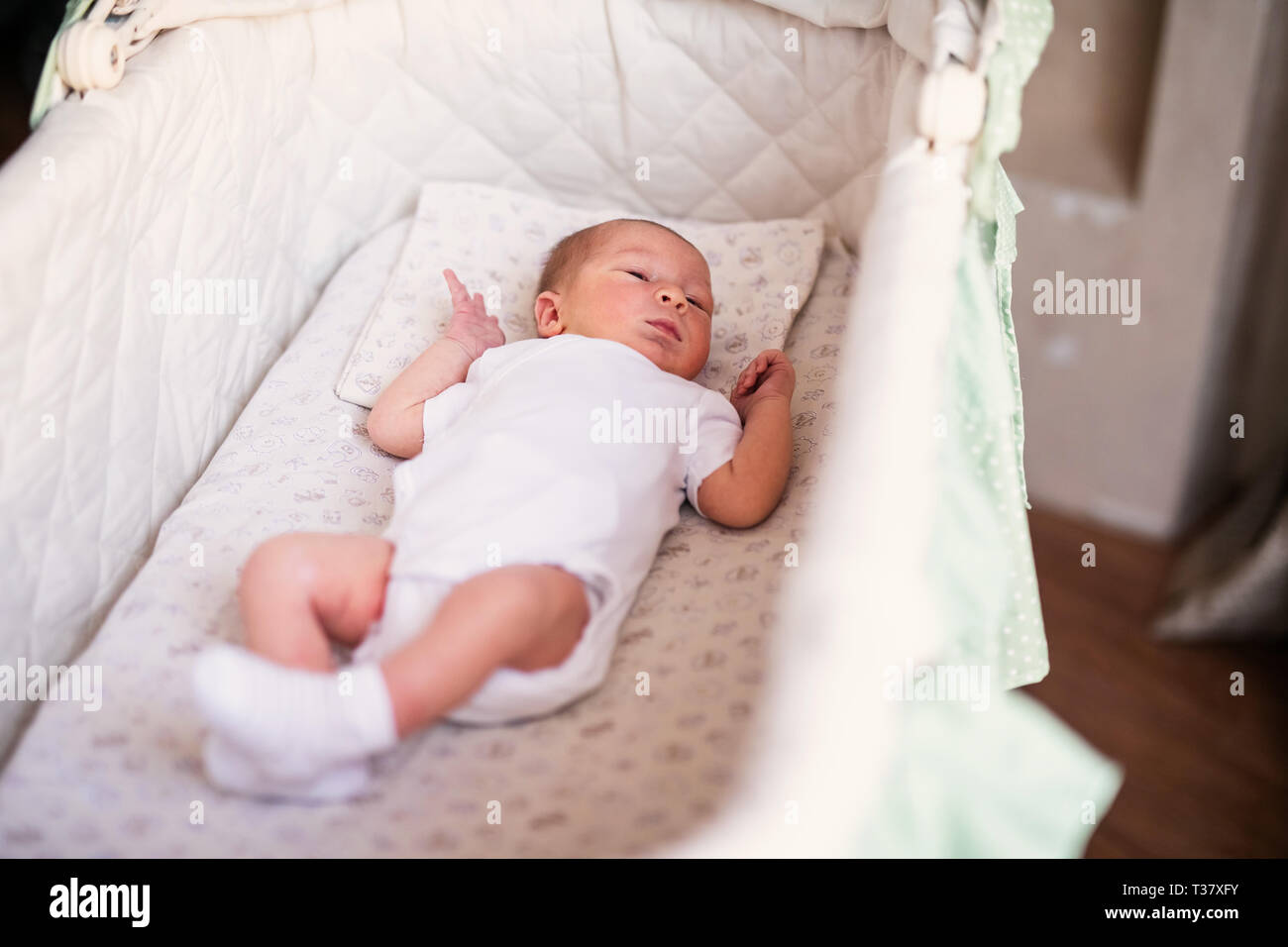 Newborn baby boy in bed. New born child in white bodykit lying in light cradle. Children sleep