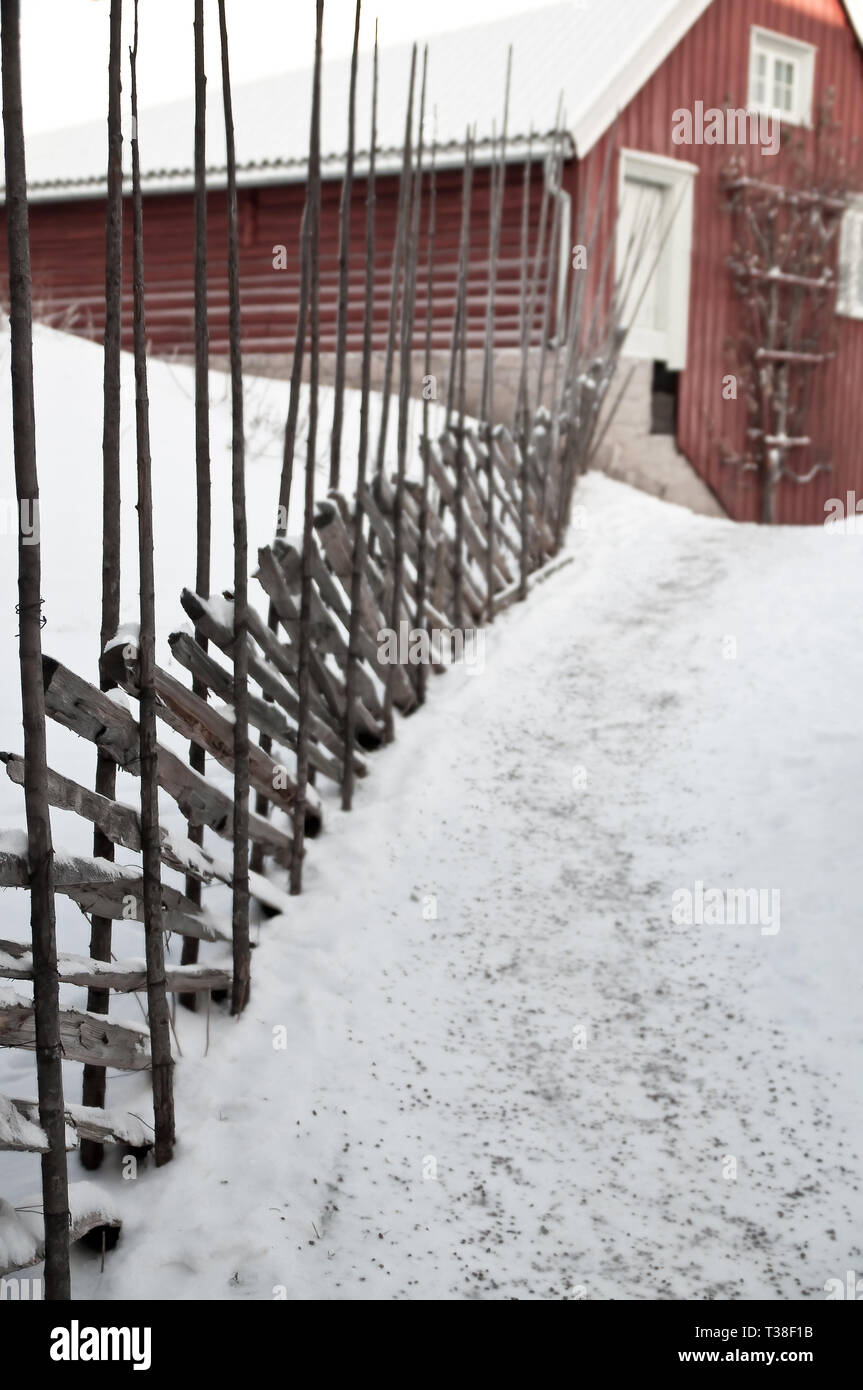 Aged agricultural red traditional barn on idyllic rural farmland, ranch road with snow and rustic old fashioned wooden log fence in the countryside Stock Photo