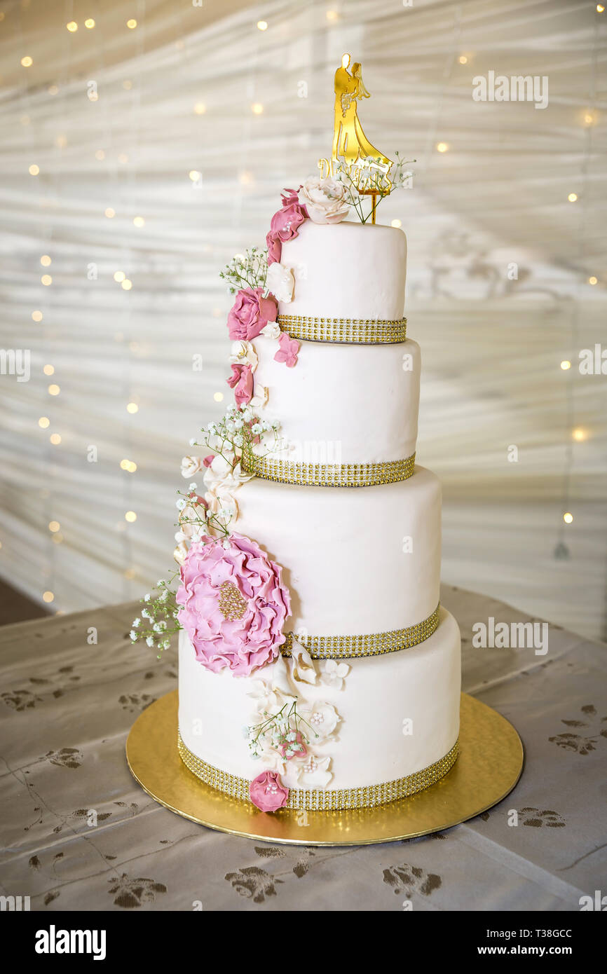 Wedding cake with white and pink sugar flowers and gold topper Stock Photo