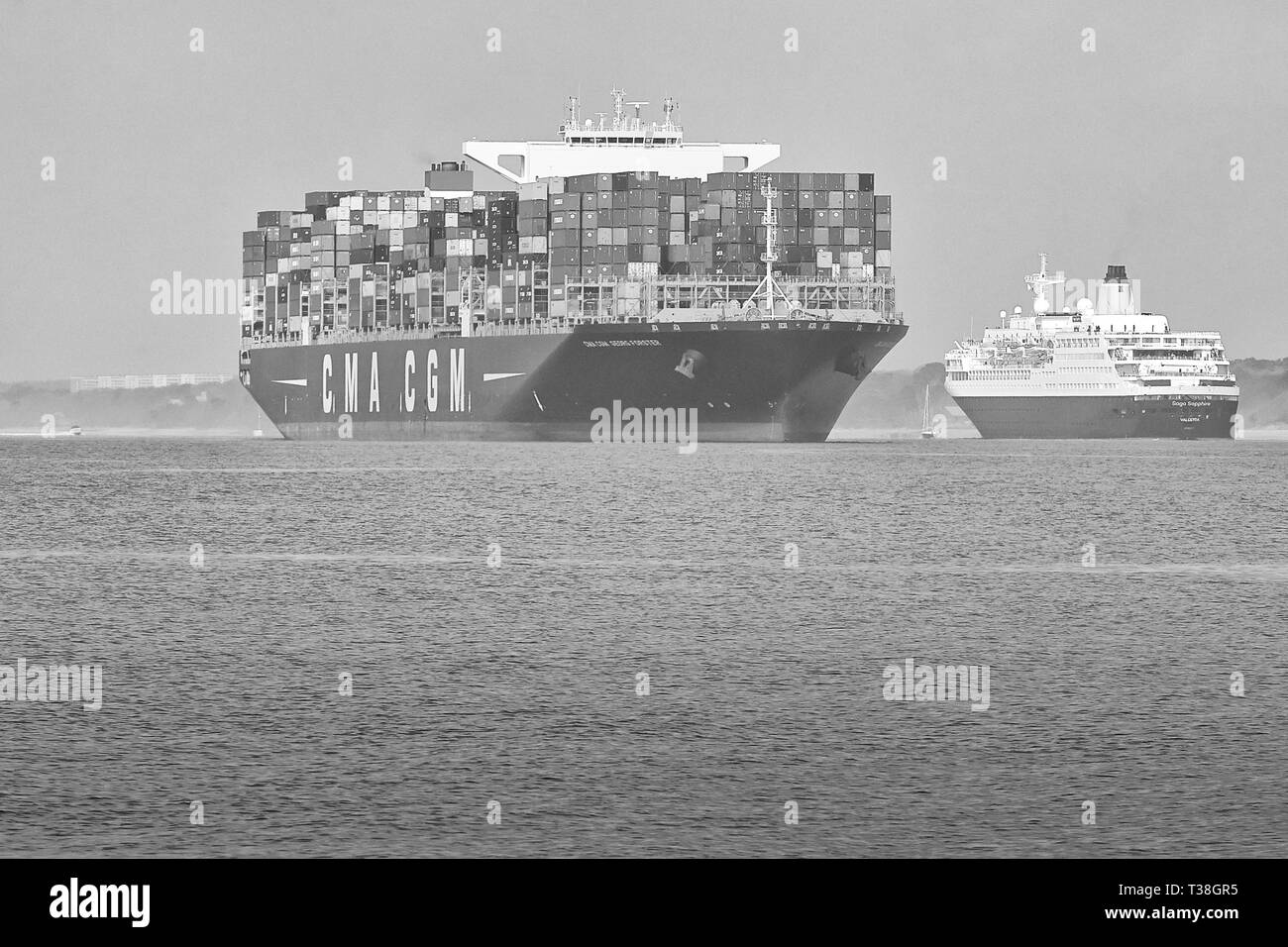 Black And White Photo Of The Container Ship, CMA CGM GEORG FORSTER, Leaving The Port Of Southampton, The SAGA SAPPHIRE Passing To Port. Stock Photo