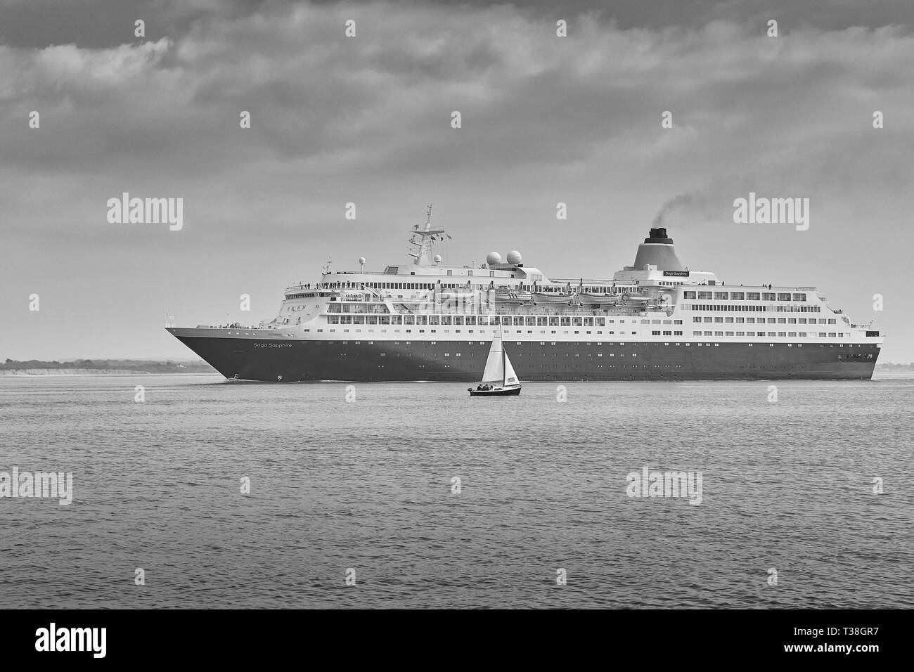 Black and White Photo Of The Saga Cruises Cruise Ship, Saga Sapphire, Approaches The Port Of Southampton, A Small Sailing Boat In Foreground. UK. Stock Photo