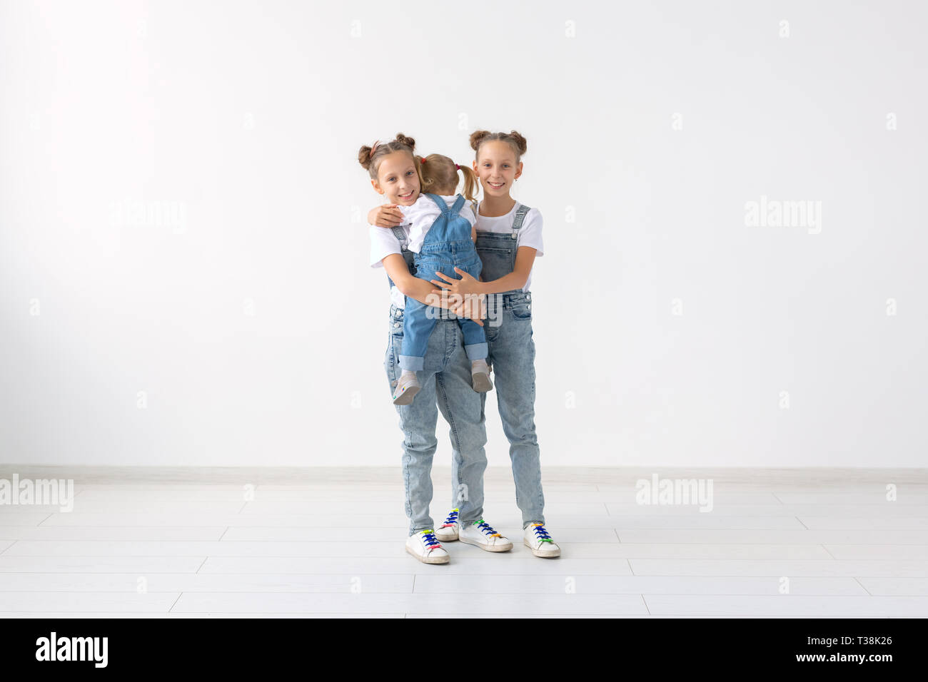 people, family and children concept - twin sisters with their baby sister in hands. Stock Photo