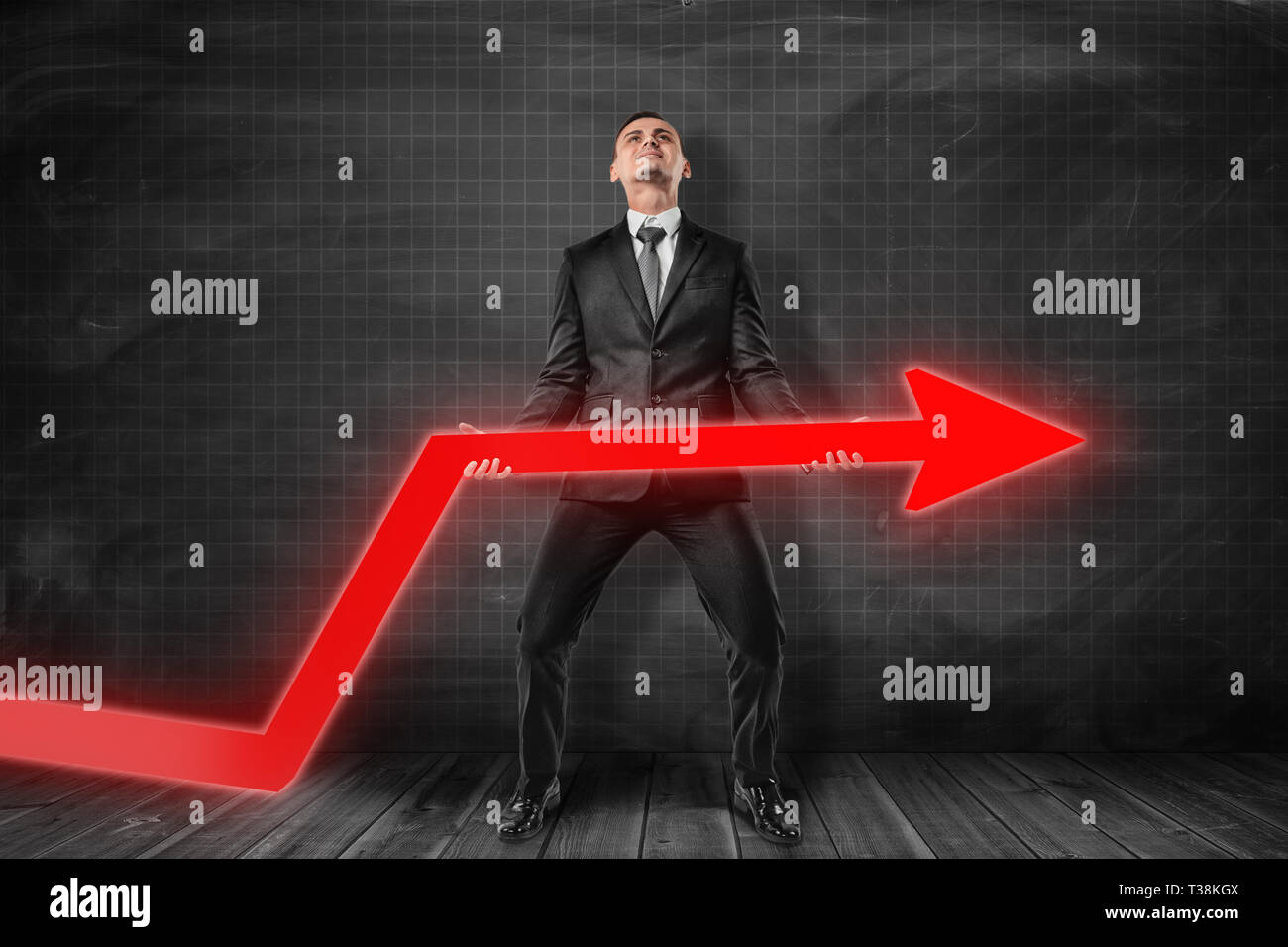 Front view of businessman standing and trying to lift up red graph ...