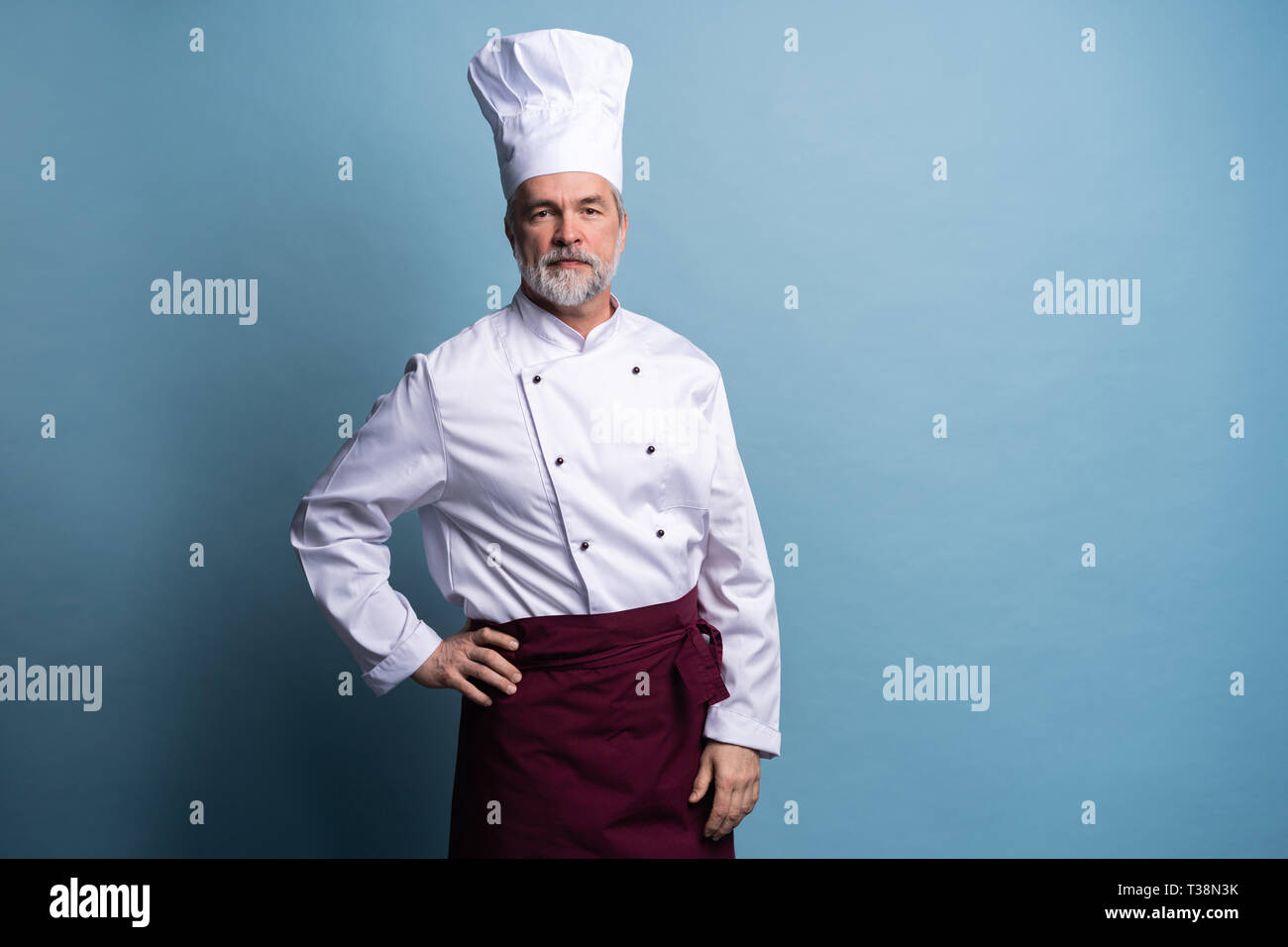 Attractive smiling cheerful chef isolated on blue. Stock Photo