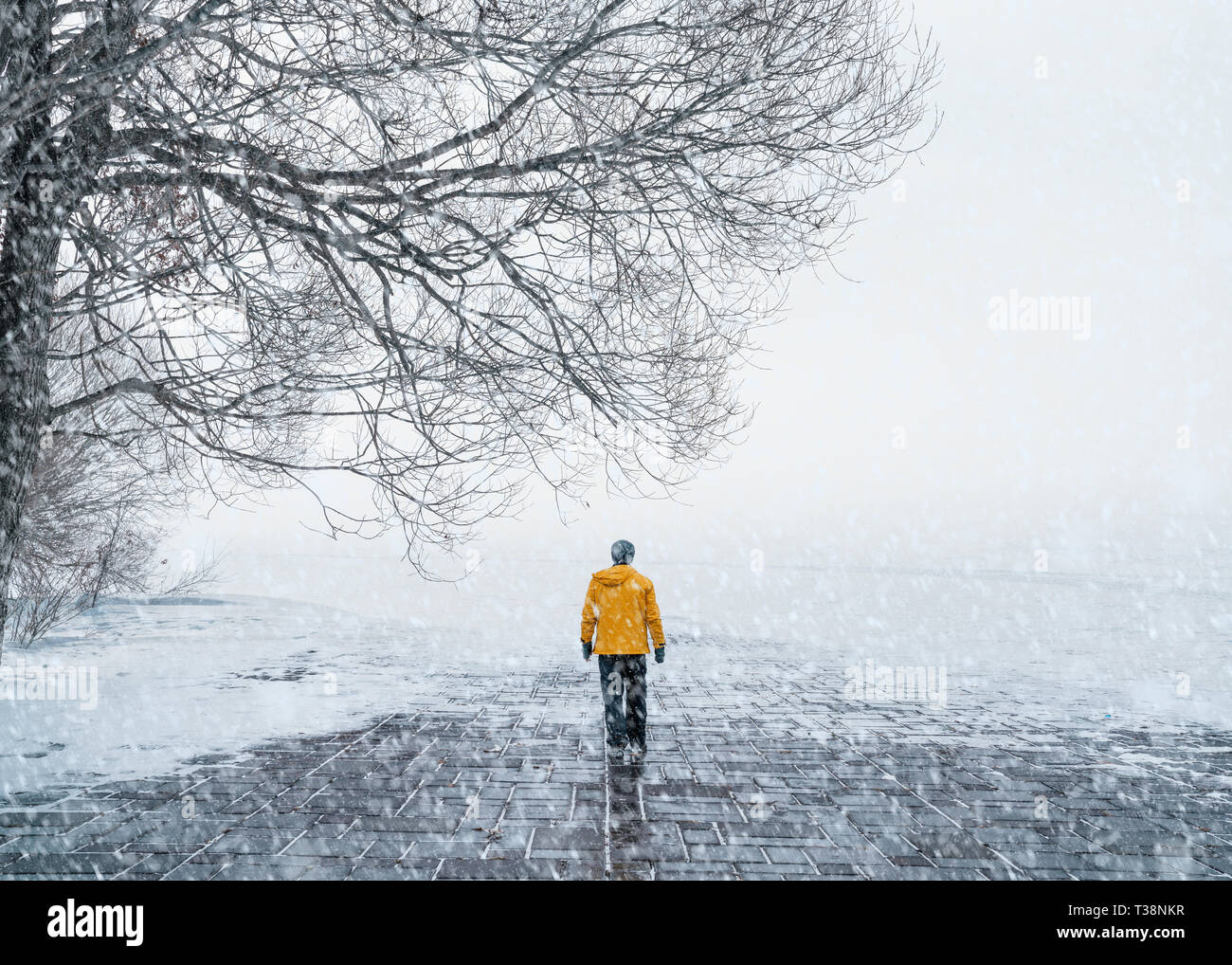 A man in a yellow coat walking on the snow-covered road Stock Photo