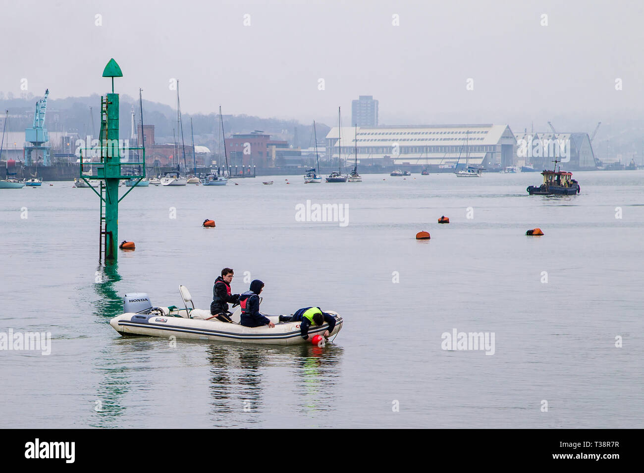 Upnor, Kent, UK. Three boys in a dinghy one grabbing hold of  a buoy. Stock Photo