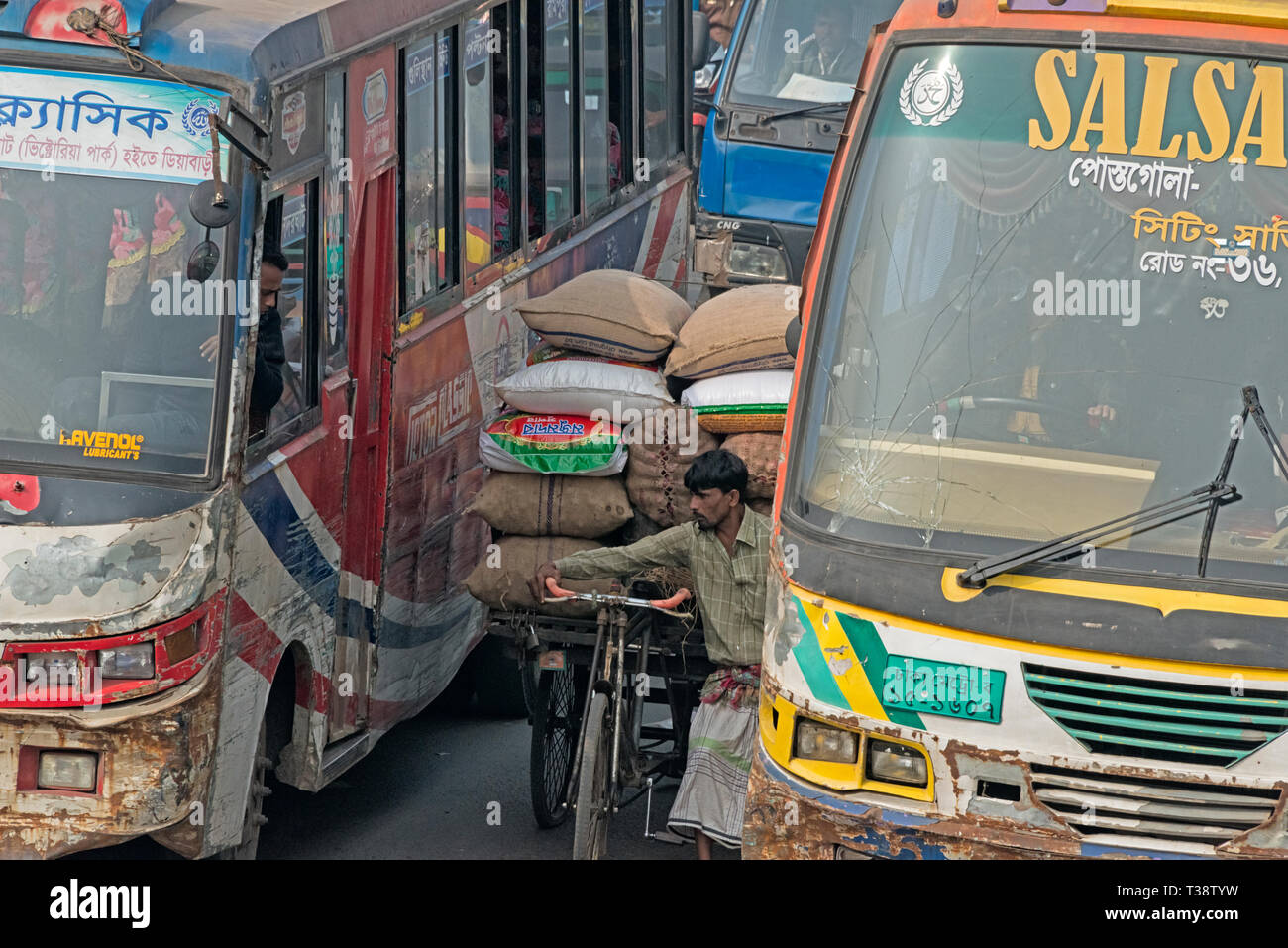 A fully loaded tricycle struggling between buses in busy traffic, Dhaka, Bangladesh Stock Photo