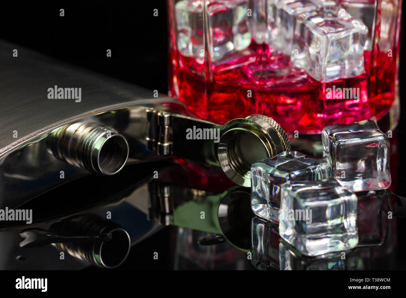 Stainless steel flask liquor alcohol and ice on table with red whiskey