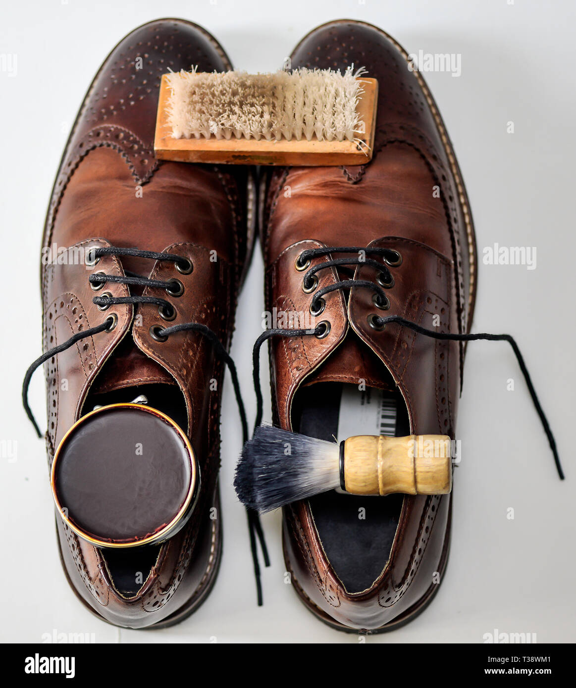 A fairly used pair of brown shoes with shoe polish, bristle brush, shoe