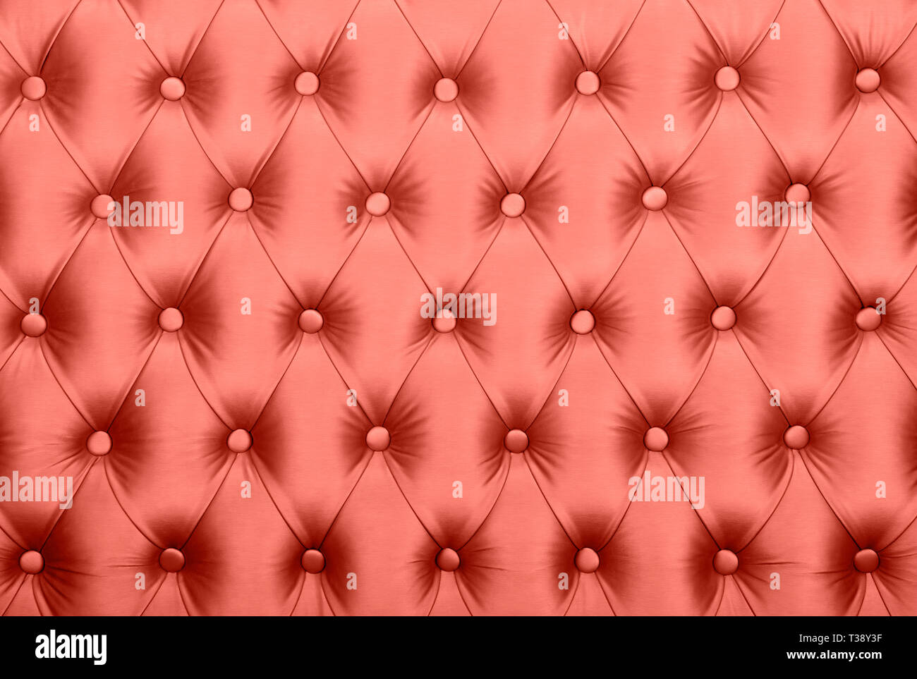 Coral toned pink leather capitone textile background, retro Chesterfield style checkered soft tufted fabric furniture decoration with buttons, close u Stock Photo