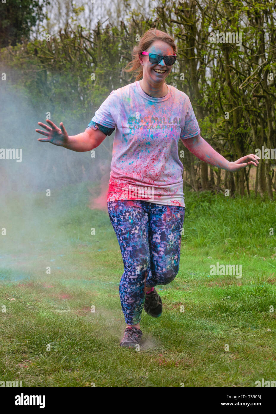 Female runner laughing and being covered in paint on Macmillan cancer charity 5K colour fun run. Stock Photo