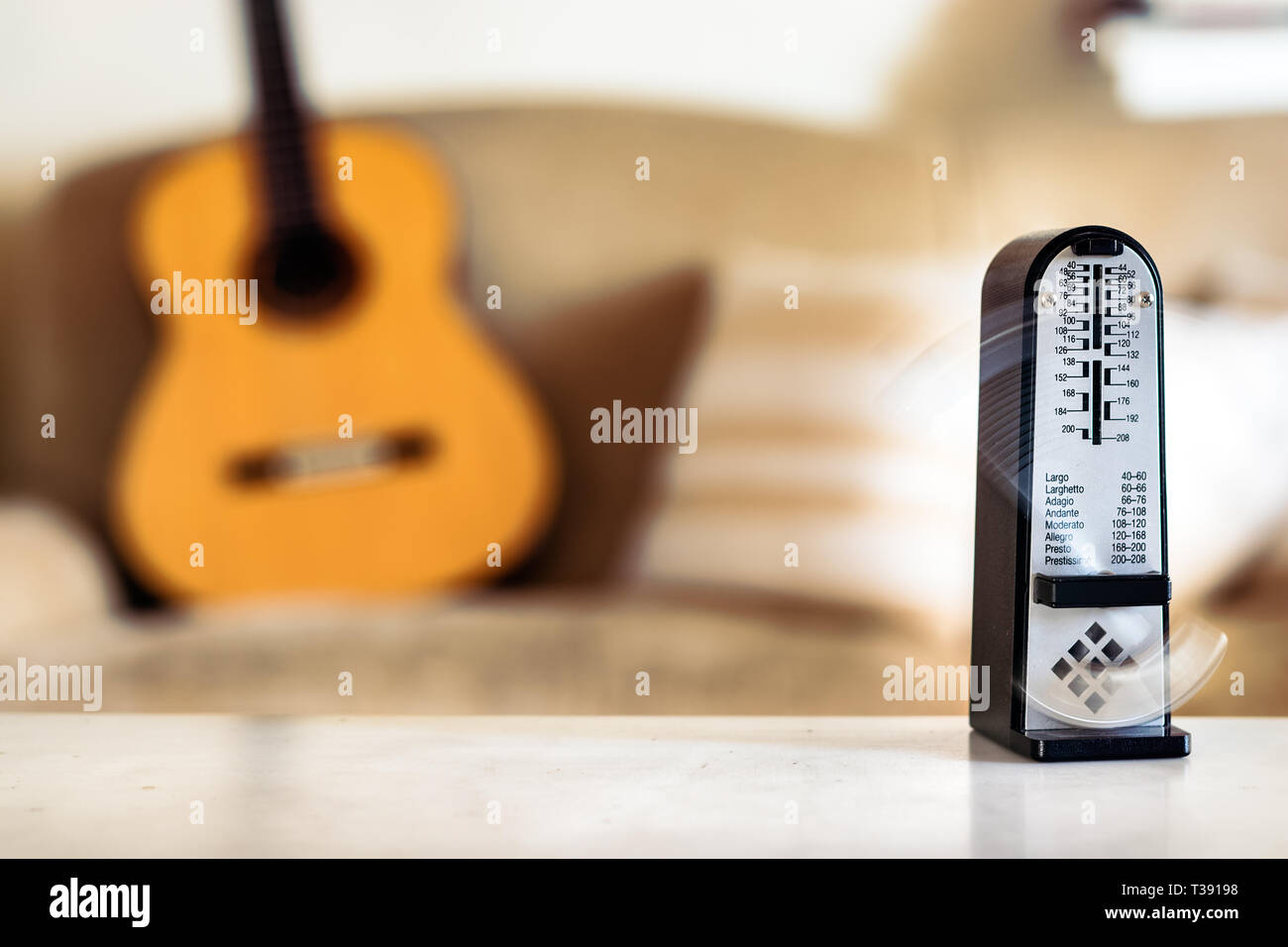 Mechanical metronome in motion, over a wooden classical acoustic guitar background Stock Photo