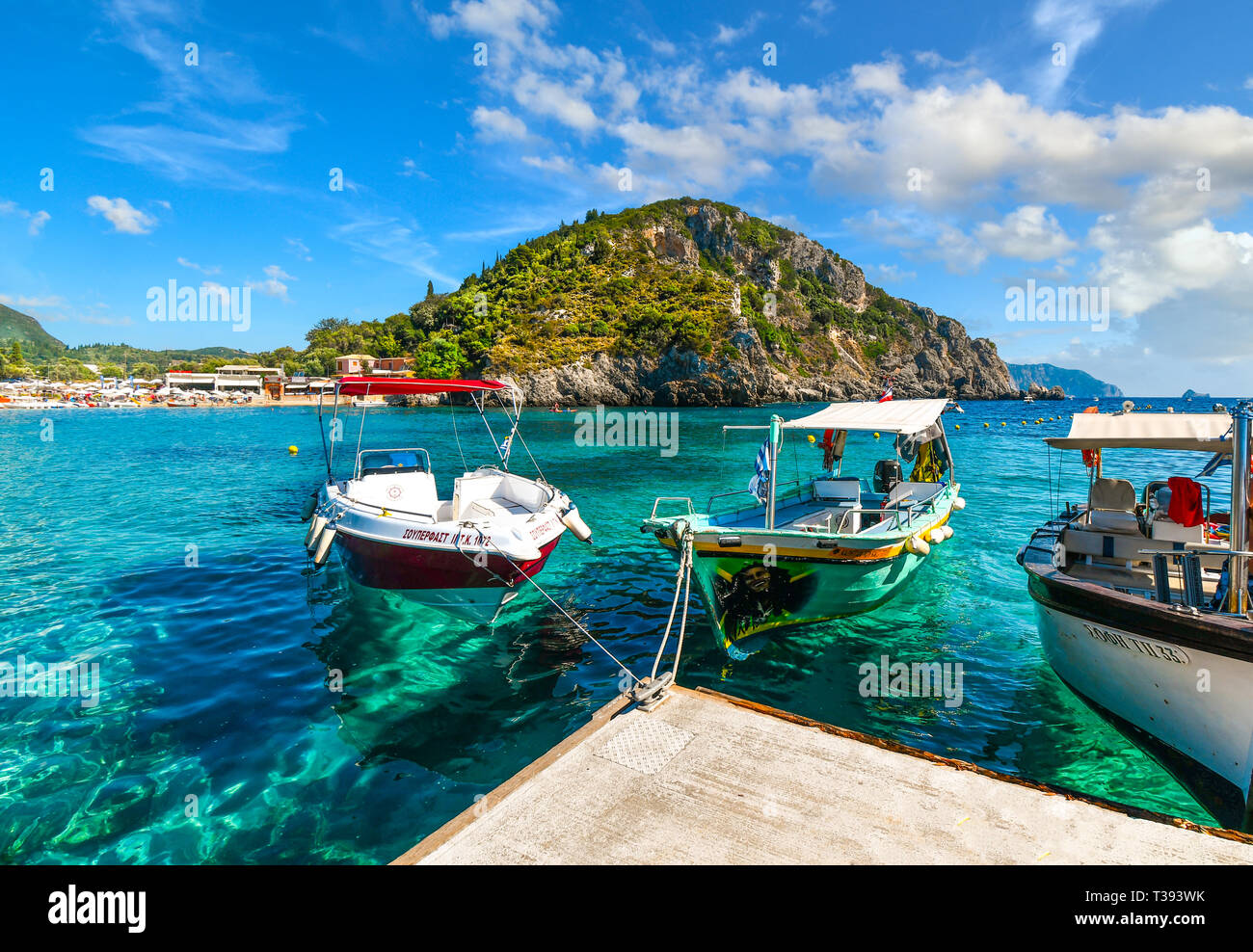 Boats docked in the crystal turquoise waters near the shore of the sandy Palaiokastritsa beach and bay on the Aegean island of Corfu, Greece. Stock Photo