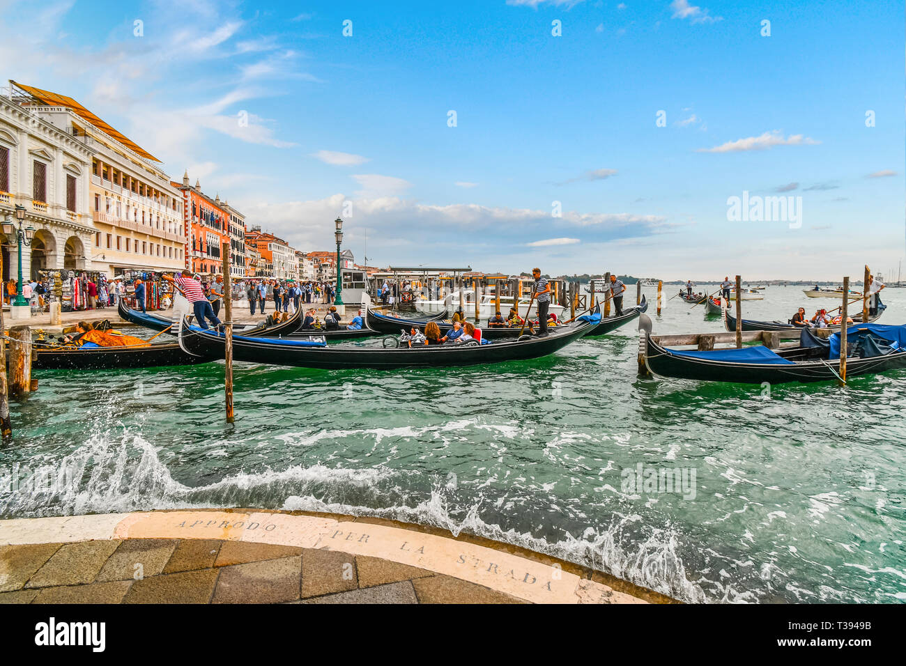 Tourists fill the gondolas at the Grand Canal station as visitors enjoy the Riva Degli Schiavoni shops and cafes along the promenade in Venice Italy Stock Photo