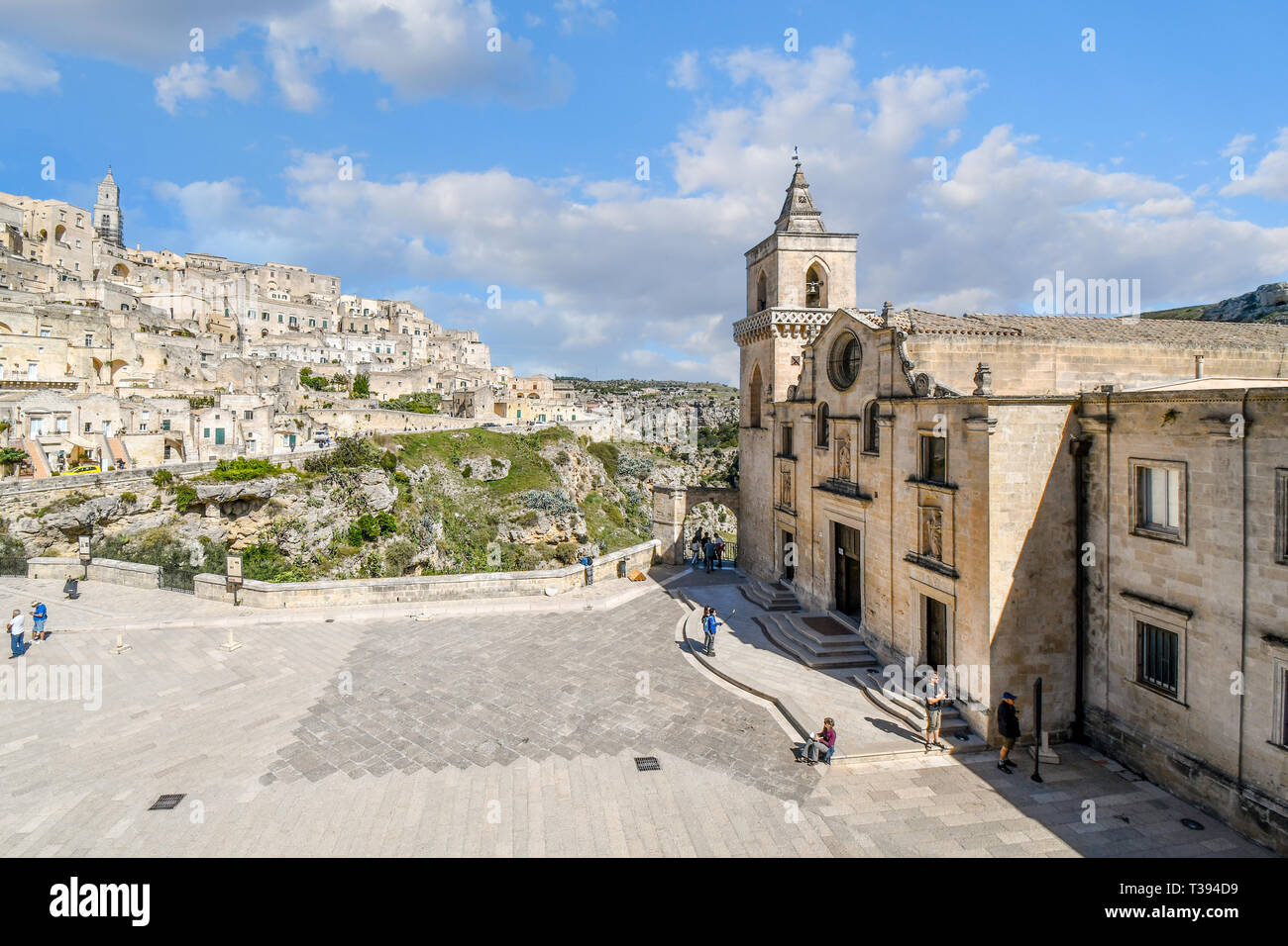 Tourists enjoy a summer day on the piazza of the Church of San Pietro Caveoso with the medieval hillside village and ancient sassi in view Stock Photo