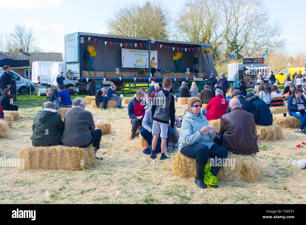 Thriplow, Cambridge, England, UK - March 2019: People attending a local country fair listening to live music sitting on hay bales Stock Photo