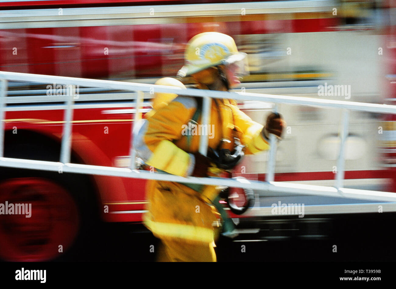 A fireman in full turnouts is carrying a ladder at a fire site, USA Stock Photo