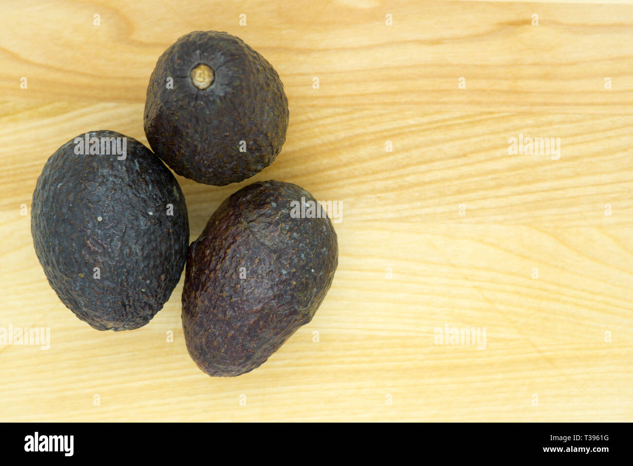 three riper avocados on a light brown table Stock Photo