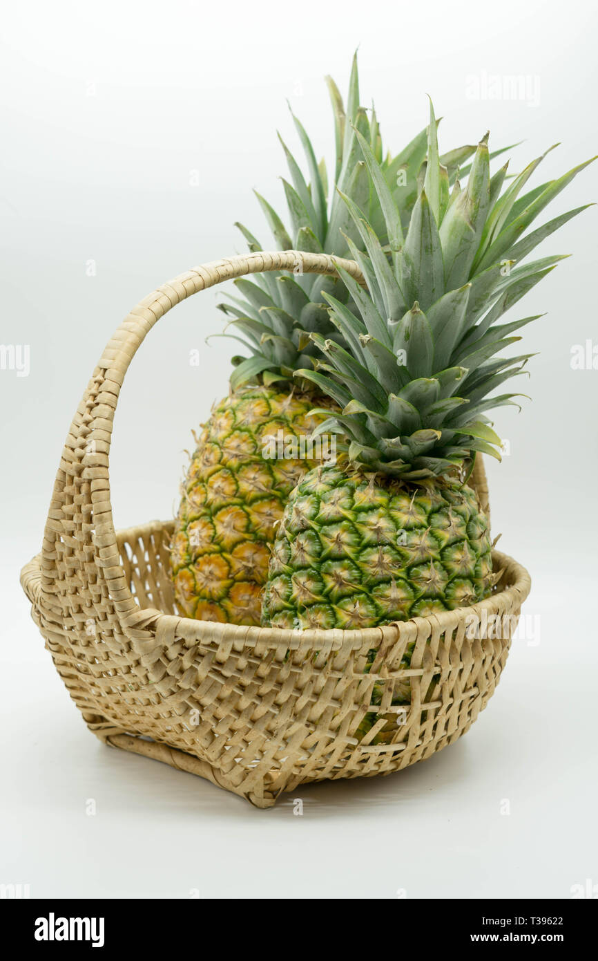 angled photo of two pineapples with large stems in a wicker basket on an isolated white background Stock Photo