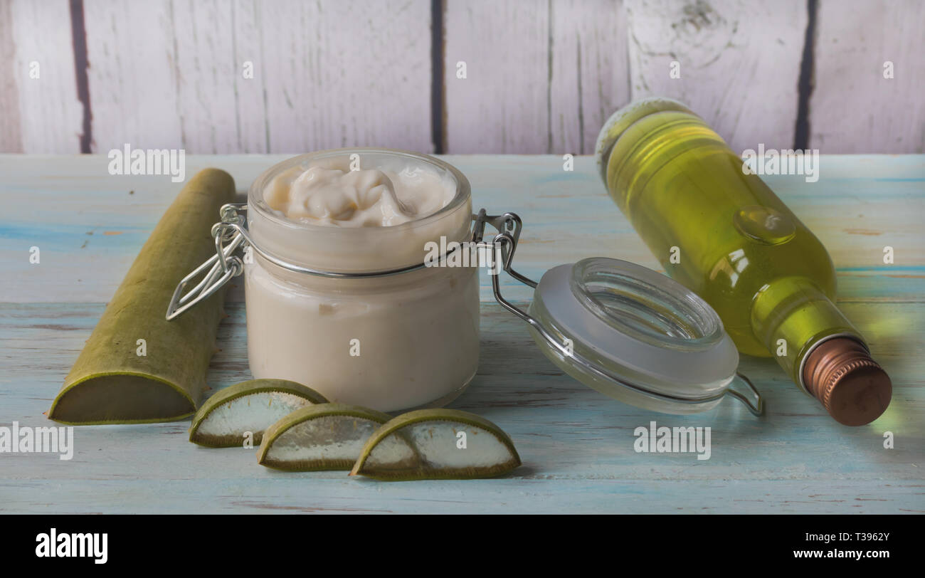 Homemade Aloe Vera cream and facial tonic in a glass jar, with cut aloe leaves on a light wood background Stock Photo