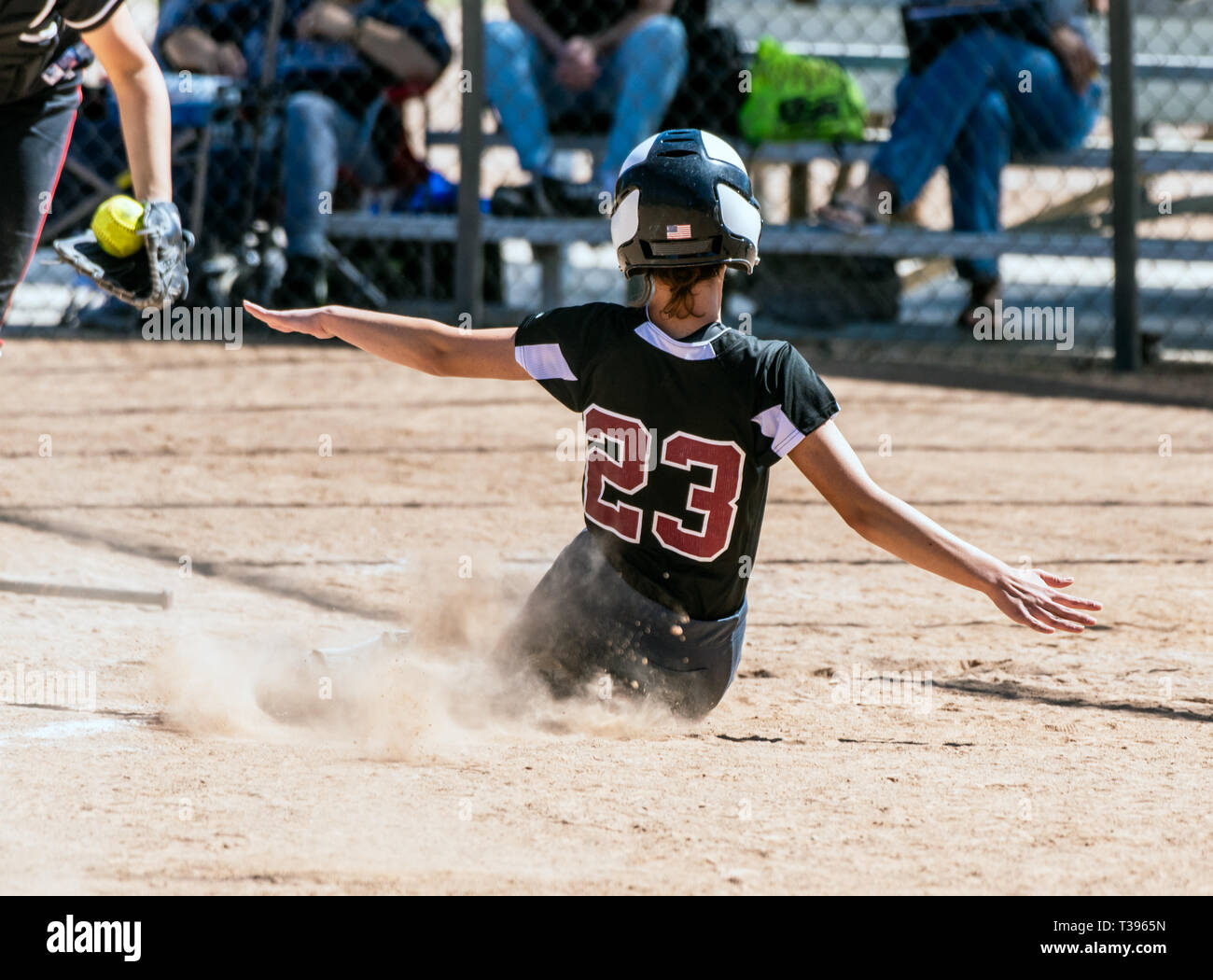 Female teenage softball player in black uniform sliding into home plate before the catcher can make the tag. Stock Photo