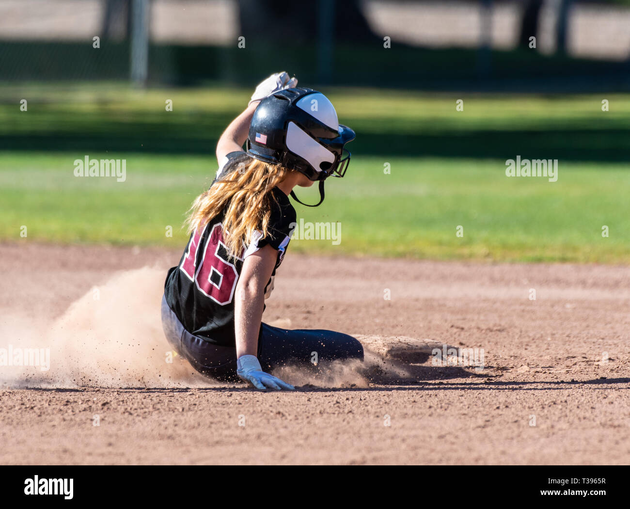 Female teenage softball player in black uniform sliding safely into second base. Stock Photo