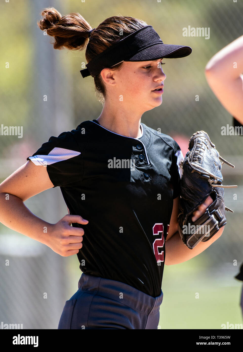 Female teenage softball player in black uniform jogging in from the field. Stock Photo