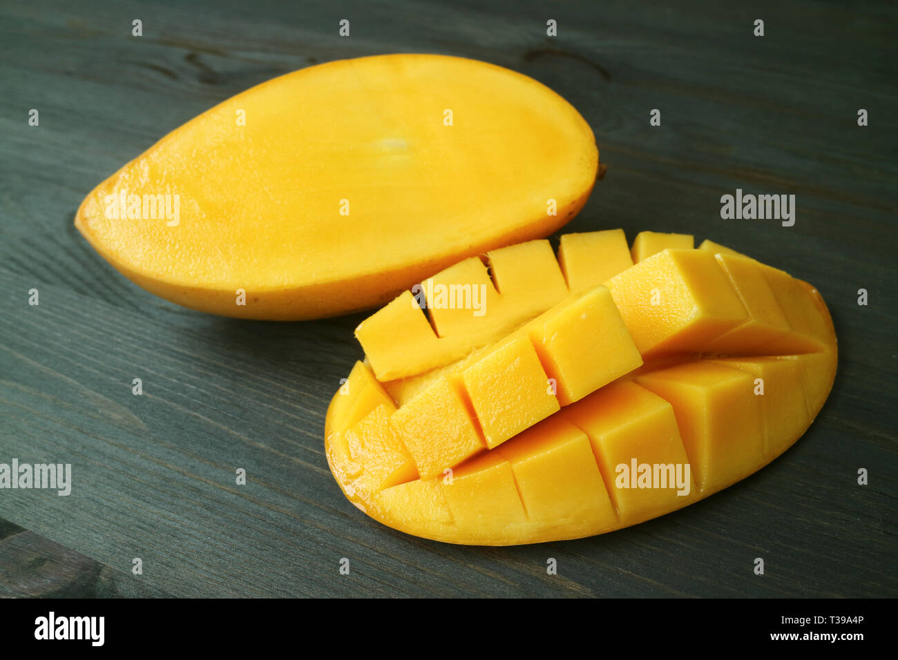 Vibrant Yellow Fresh Ripe Thai Nam Dok Mai Mango Cut in Half on Dark Brown Wooden Table Stock