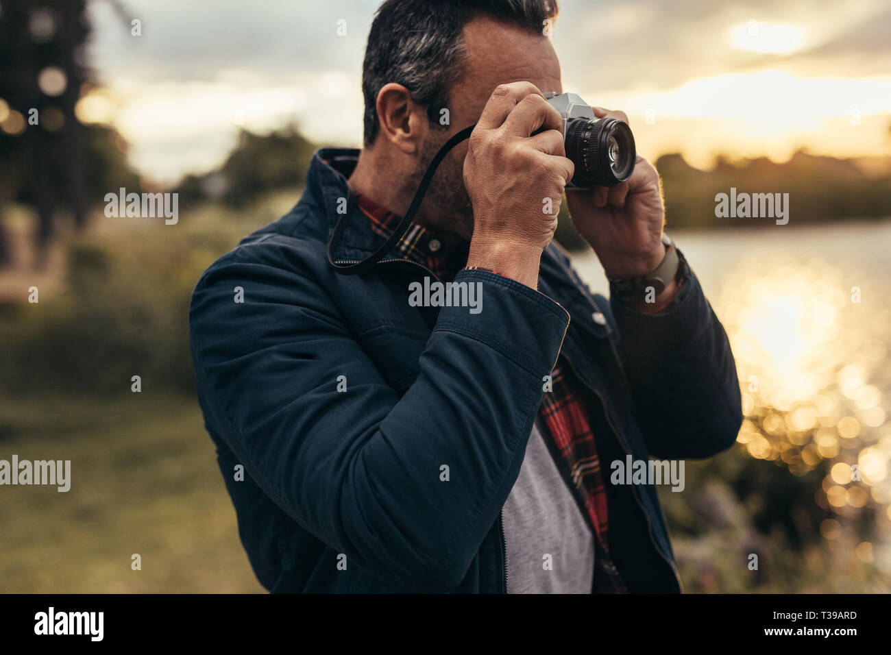 Close up of a man standing near a lake taking photos of nature. Nature lover capturing the beauty of nature in a camera. Stock Photo