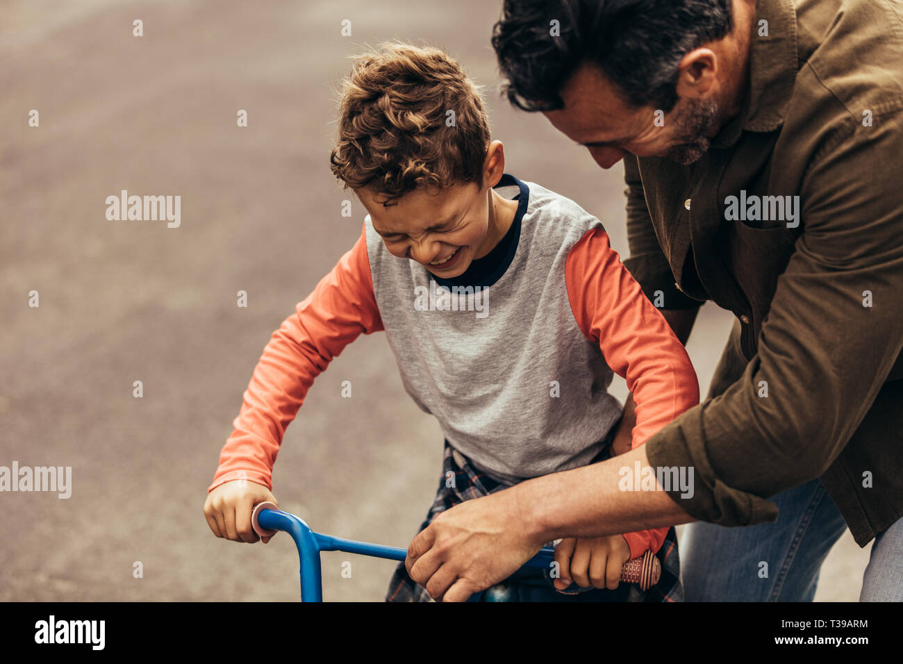 Man holding the bicycle while his son learns to ride it. Boy excited to ride a bicycle. Stock Photo