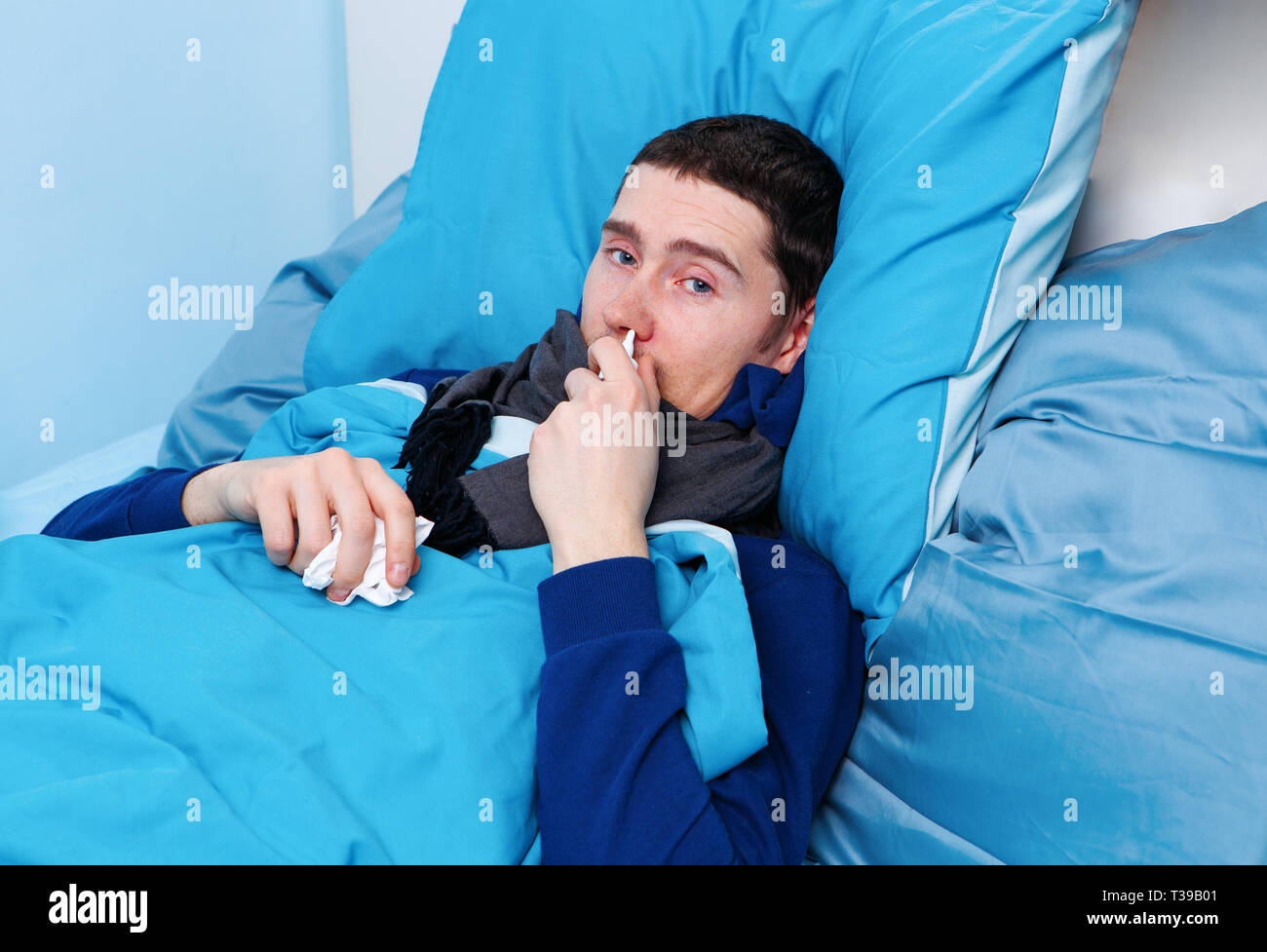 Image of sick brunet man using nasal spray while lying in bed Stock Photo