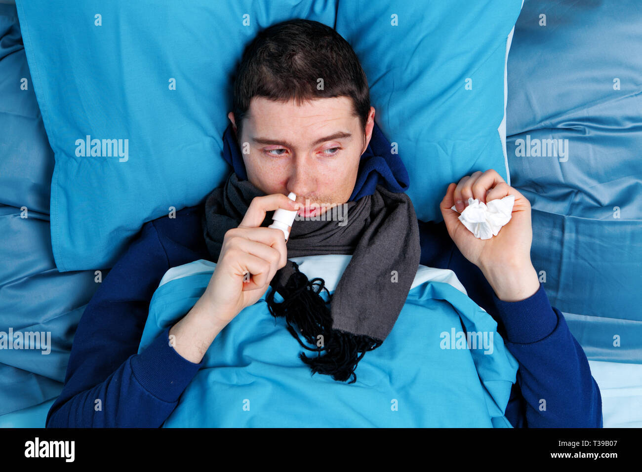 Sick brunet man using nasal spray while lying in bed Stock Photo