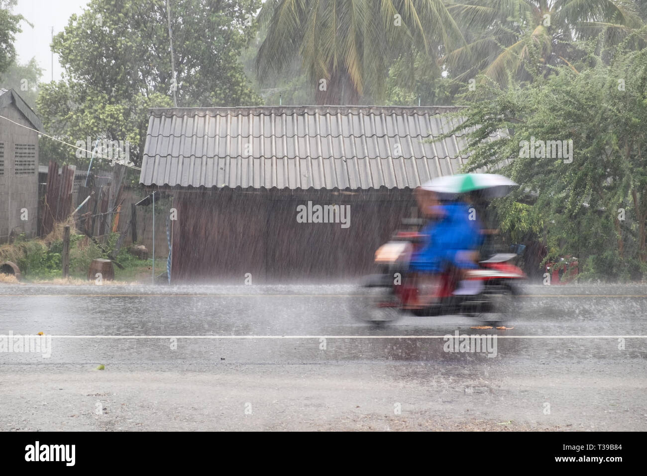 Motorcycle motion riding thourgh gale rain on front wooden house in road community Stock Photo