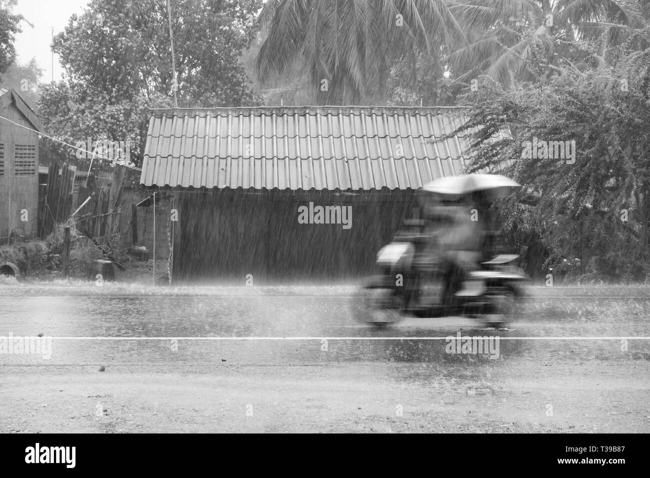 Motorcycle motion riding through gale rain on front wooden house in road community,black white,bw Stock Photo