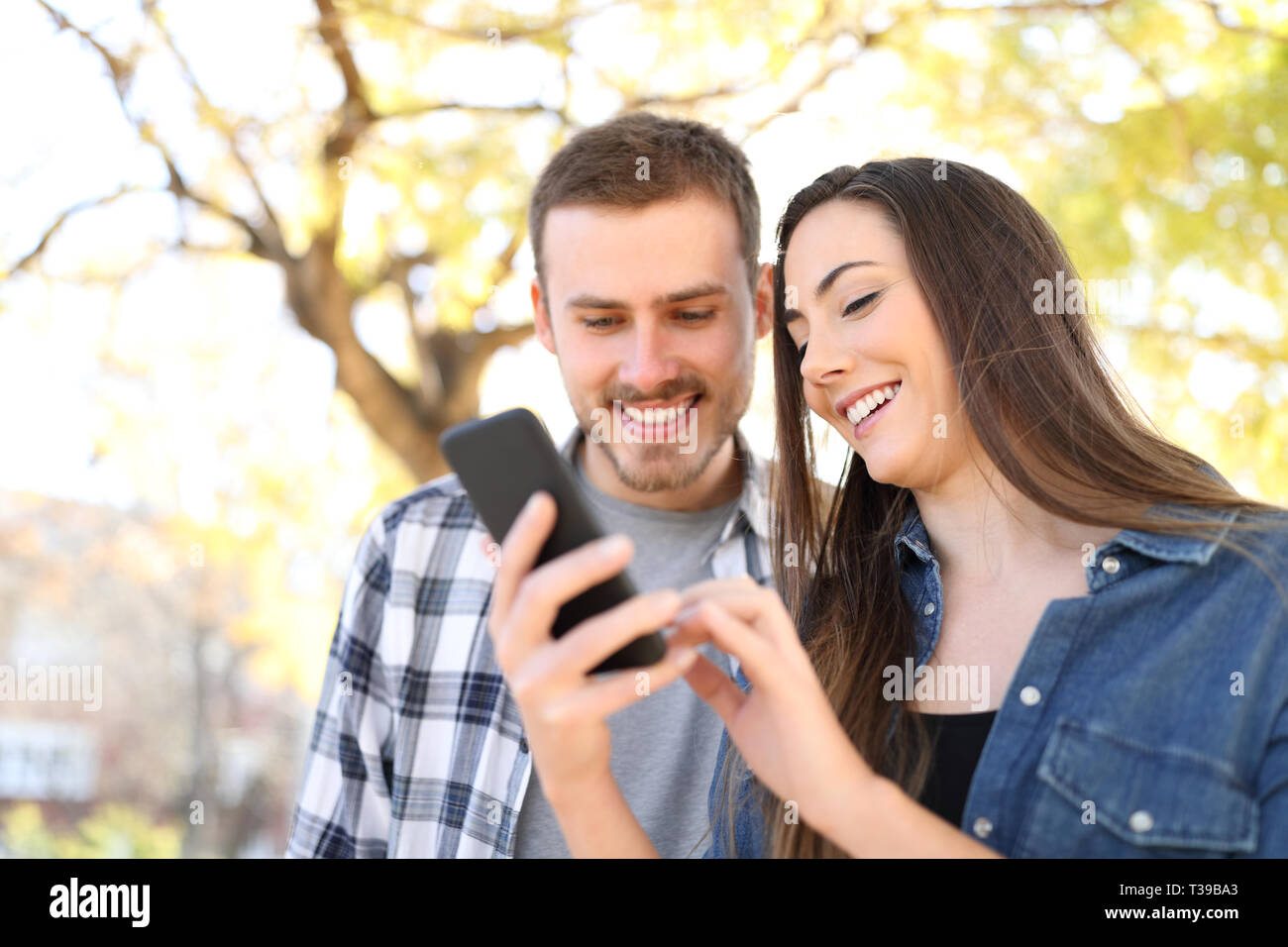 Happy couple in a park using a smart phone checking online content Stock Photo
