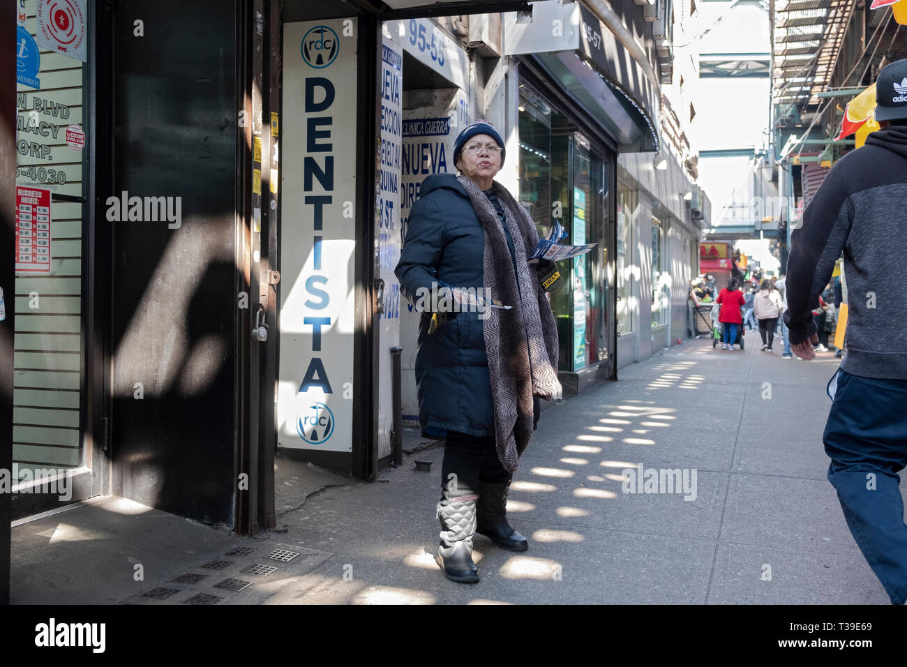 A Latin American woman hands out leaflets for a Spanish speaking dentist under the elevated subway in Corona, Queens, New York City. Stock Photo