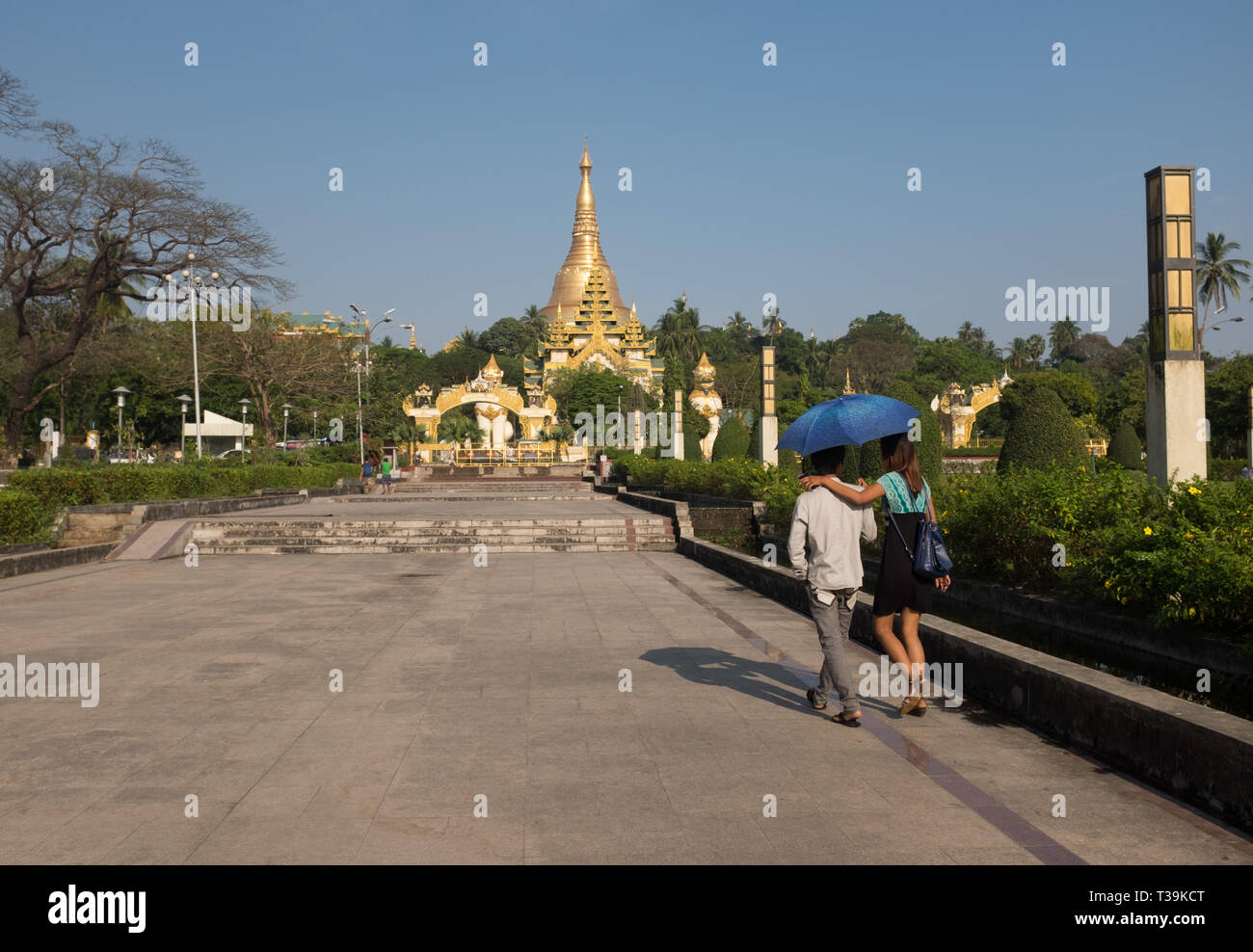 Young couple holding an umbrella walking in the People's Park & People's Square, in the background the Shwedagon Pagoda, Yangon, Myanmar (Burma) Stock Photo