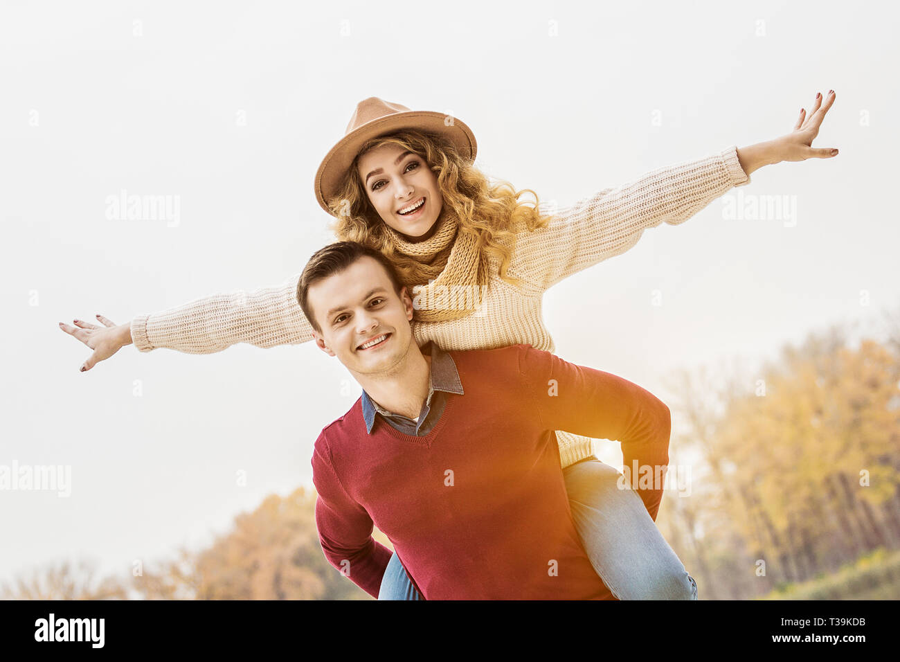 Enjoy every moment together. Low-angle view of cheerful woman keeping arms outstretched while piggybacking her boyfriend. Young man carrying beautiful Stock Photo