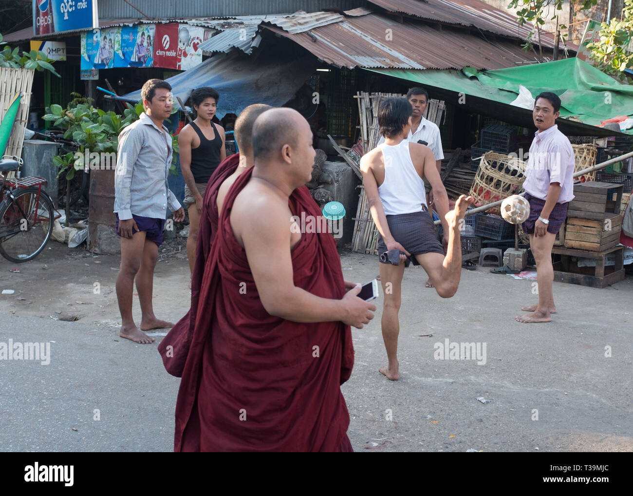 Two monks walking past men playing Chinlone also known as caneball, is the traditional, national sport of Myanmar (Burma). It is non-competitive, with Stock Photo