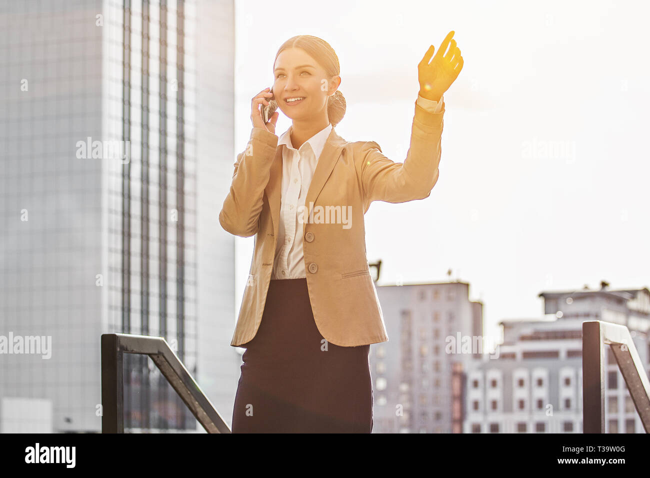 Business dialog on the phone. Low-angle view of beautiful and young business woman in smart casual clothing talking on the phone and keeping arm raise Stock Photo