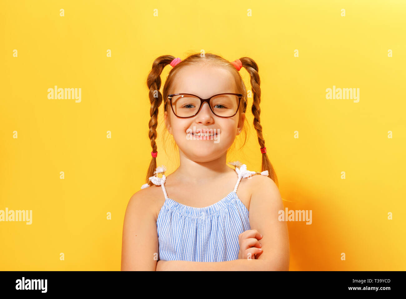 Portrait of a funny little girl of preschool child with glasses on a yellow background. Stock Photo